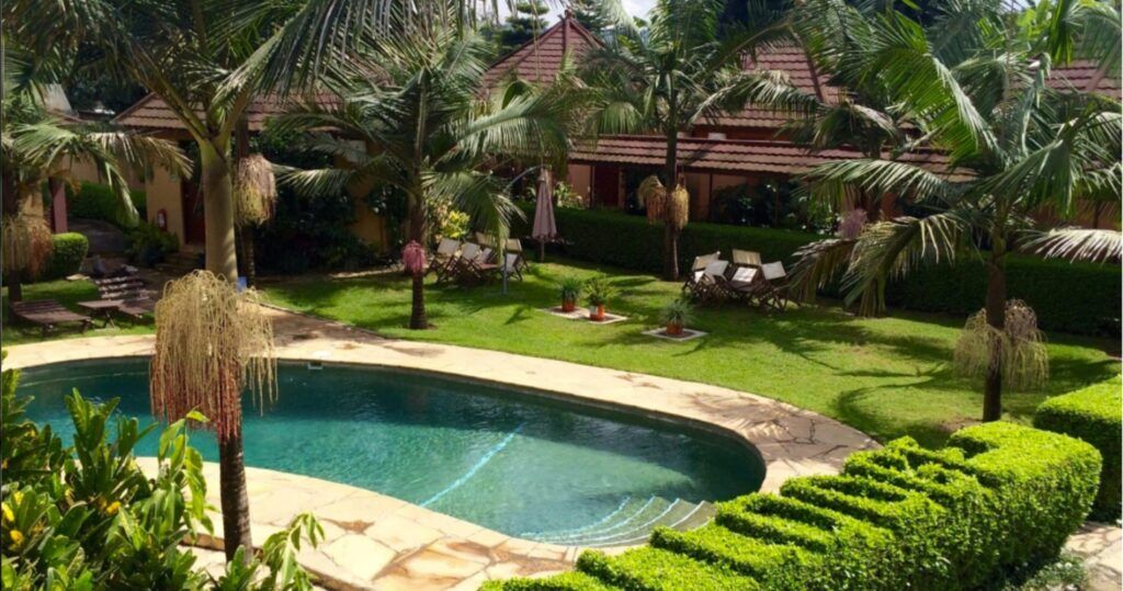 Pool in a green garden with palm trees and houses around