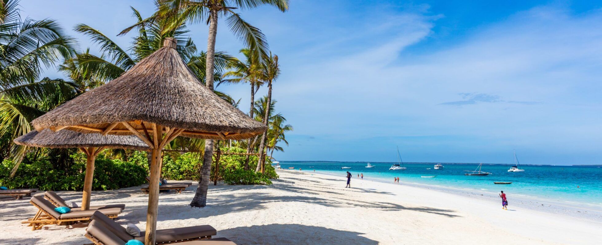 Four sunbeds and two palm parasols at the white beach with palm trees