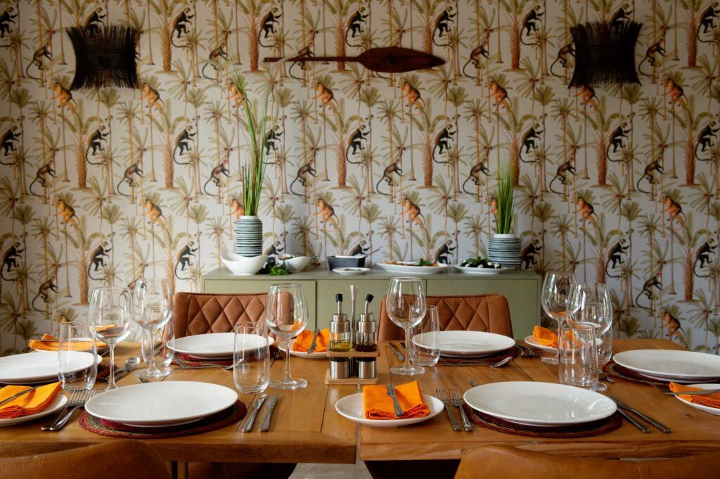 Wooden table with plates, cutlery, glasses and orange napkins and a wallpaper with monkeys 