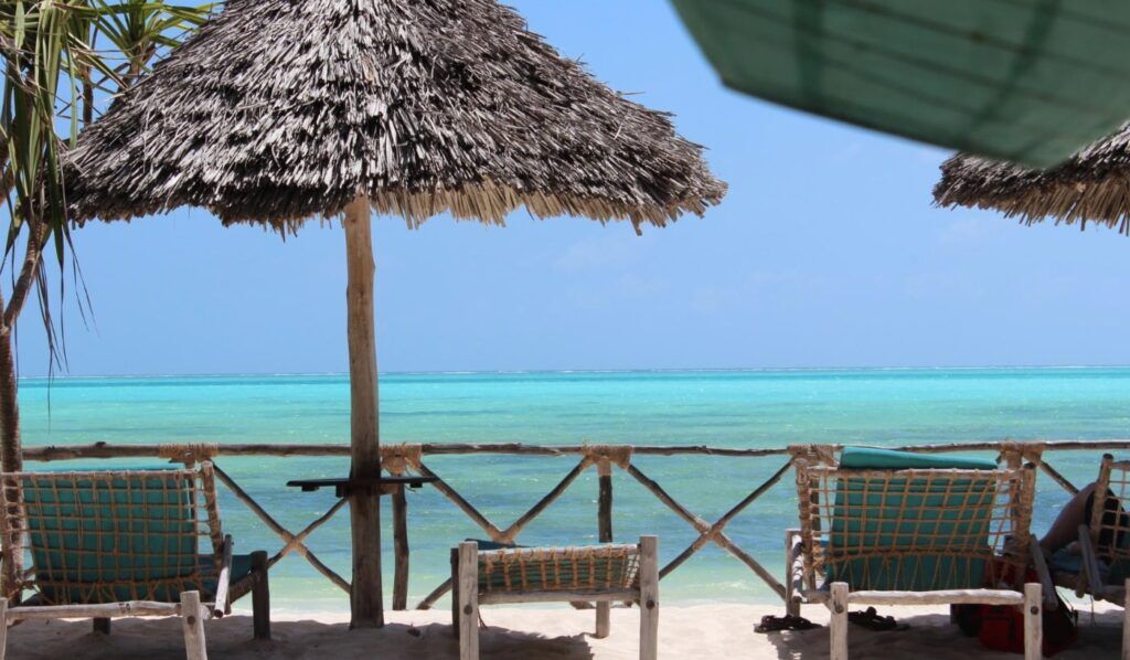 Sunbeds and a parasol in front of a wooden fence and the Indian Ocean