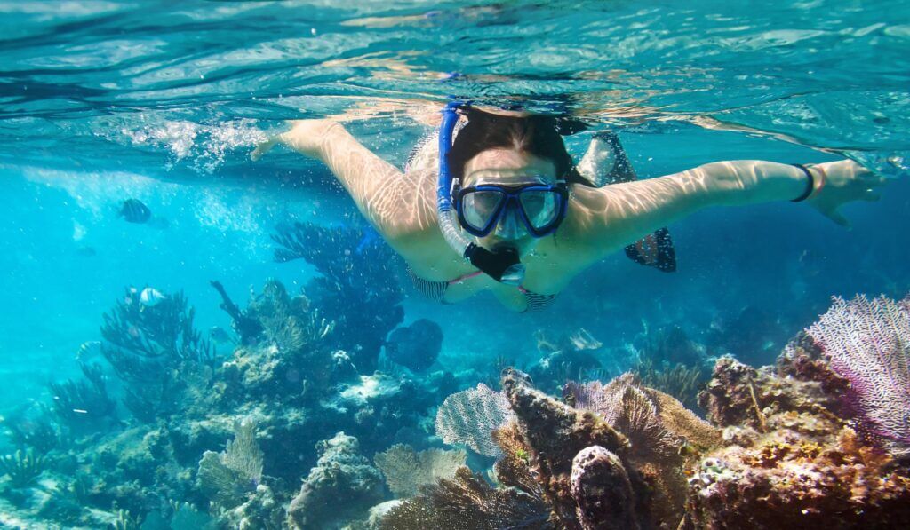 Woman with snorkel and diving goggles under water close to corals