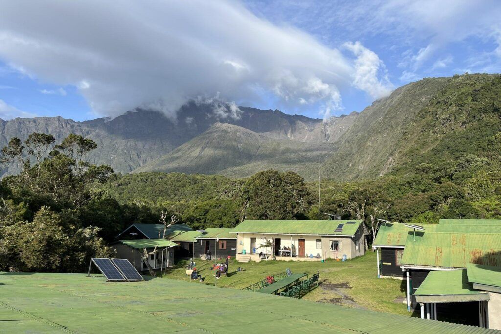 Miriakamba Huts of Mount Meru with green roof surrounded by the mountain, trees and green fields