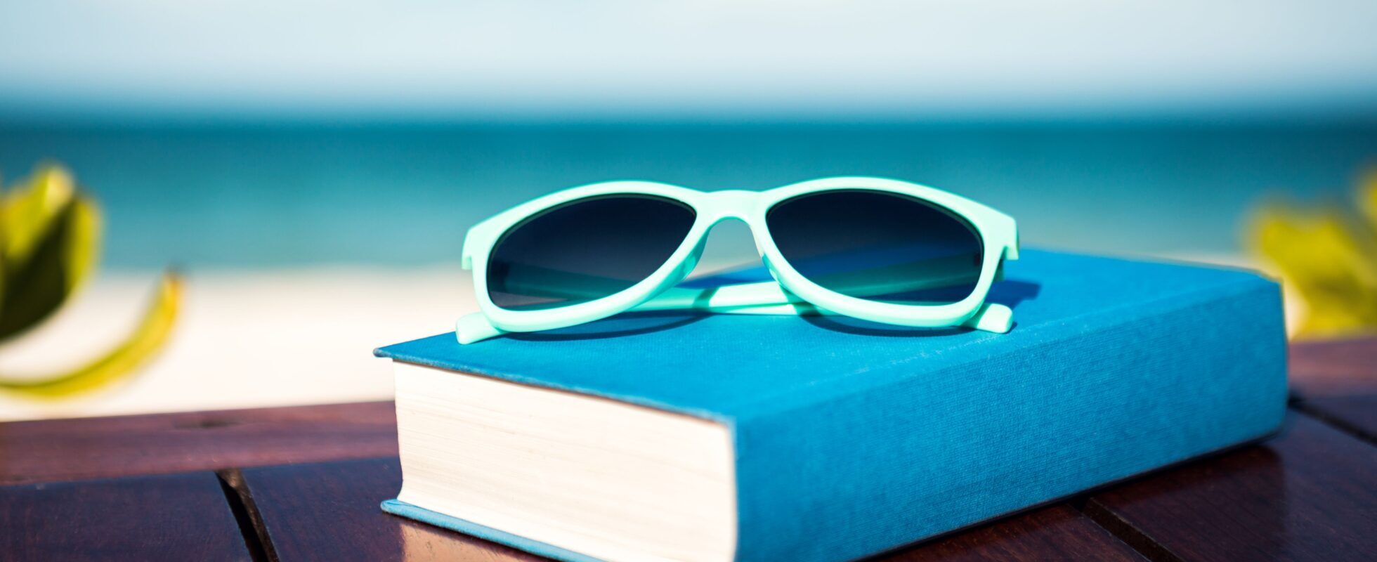 A book and sunglasses on a table with the beach in the background